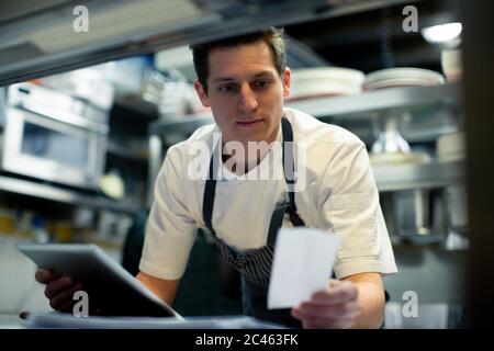 Young male chef using digital tablet and reading food order in kitchen Stock Photo