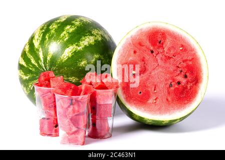 sliced red watermelon cubes in plastic cup a front of Fresh organic green watermelon and sliced half of watermelon with red texture. Stock Photo