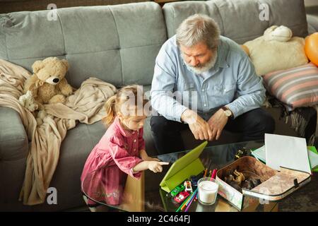 Grandfather and grandchild playing together at home. Happiness, family, relathionship, learning and education concept. Sincere emotions and childhood. Reading books, playing gadgets, look happy. Stock Photo