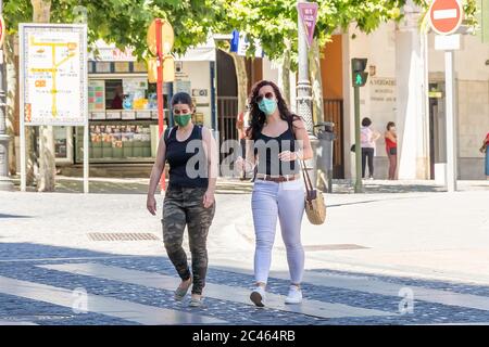 Jaen, Spain - June 18, 2020: Two women crossing by crosswalk wearing protective or medical face masks during the alarm state and quarantine in Spain. Stock Photo