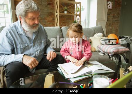 Grandfather and grandchild playing together at home. Happiness, family, relathionship, learning and education concept. Sincere emotions and childhood. Reading books, fairytails, poems, look happy. Stock Photo
