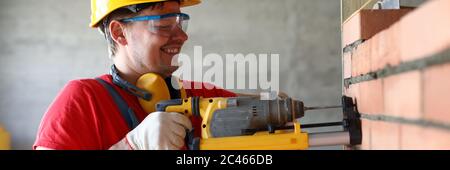 Builder drilling hole in wall, construction site Stock Photo