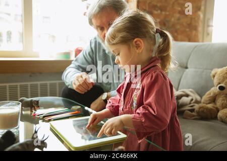 Grandfather and grandchild playing together at home. Happiness, family, relathionship, learning and education concept. Sincere emotions and childhood. Reading books, drawing, playing with puzzles. Stock Photo