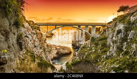 The Ciolo bridge connects two high cliffs. An inlet of the sea, in Gagliano del Capo, near Santa Maria di Leuca. The red and orange sunset. Salento, P Stock Photo