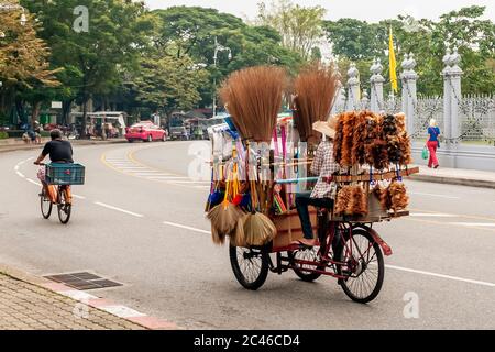 Street vendor of brooms and feather dusters travels a street in central Bangkok, Thailand, with the rickshaw full of goods Stock Photo