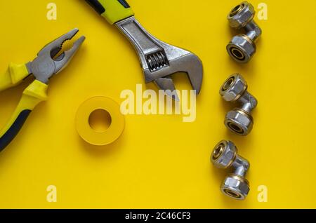 Yellow background with hand tools, Teflon tape and plumbing fittings. Adjustable wrench, pliers, PTFE tape and three bronze corner fittings for multil Stock Photo