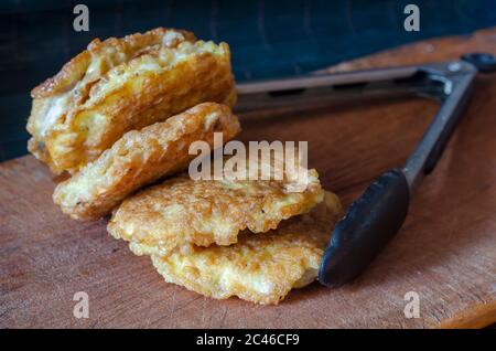 Fried chops in batter on a wooden cutting board. Kitchen tongs and a serving of fried chops. The process of preparing meat dishes. Close-up. Selective Stock Photo