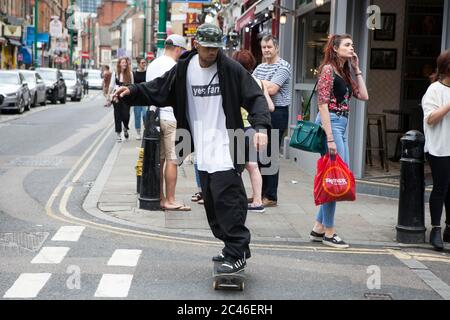 London, UK - 17 July 2019, A man in a long black cardigan rides on a skateboard along the street. Stock Photo