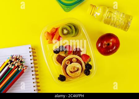 Delicious food in container and colorful pencils on yellow background. Back to school concept. Stock Photo