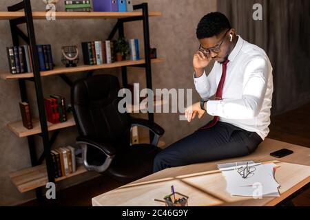 Portrait of serious African American man in glasses looking to the watch in the office  Stock Photo
