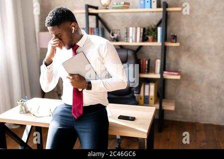 Handsome young african american guy in glasses sitting at table and tired from work Stock Photo
