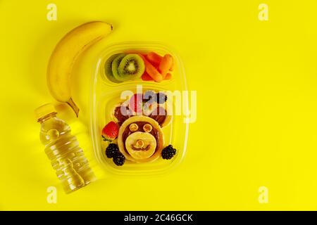 Tasty food in lunch boxes with water and banana on yellow background. Stock Photo