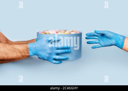 Men's hands in latex gloves give a box of flowers to the woman's hand in a medical glove. Stock Photo