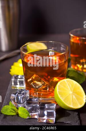 Fresh cocktail Cuba Libre or whiskey cola cocktail with brown rum, cola, mint and lime on black background. Long Island Iced Tea cocktail. Stock Photo