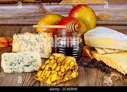 Different types of cheese with jar of honey on wooden background. Stock Photo