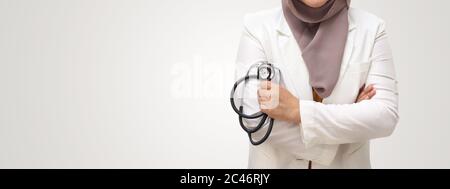 Muslim female doctor wearing hijab and suit, standing with crossed arm and holding stethoscope, succesful confident person, on white background Stock Photo