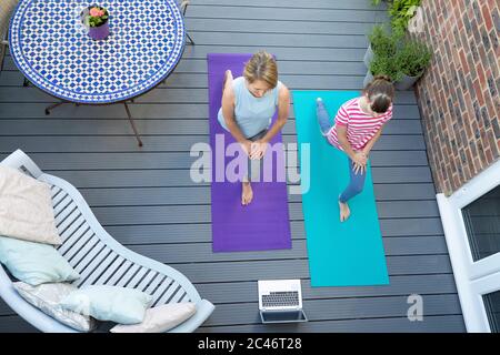 Overhead View Of Mother And Daughter Following Online Exercise Class On Laptop At Home On Deck Stock Photo