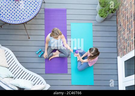 Overhead View Of Mother And Daughter Giving Each Other Cheers With Water Bottle After Exercising Together At Home On Deck Stock Photo