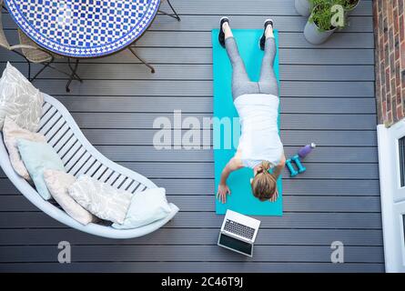 Overhead View Of Healthy Mature Woman Following Online Exercise Class On Laptop At Home On Deck Stock Photo