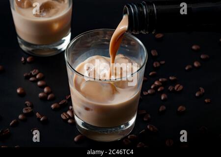 Pouring irish cream in a glass with ice, surrounded by coffee beans on a dark black background Stock Photo