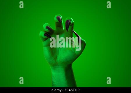 Halloween, nightmare creature and evil monster horror story concept with a scary zombie or demon hand with creepy long black nails isolated on green w Stock Photo