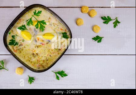 Creamy spinach soup in black bowl with egg and crackers on white wooden background. Stock Photo