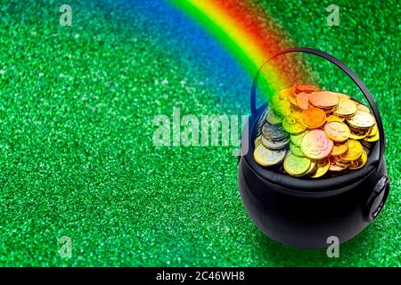 Saint Patrick's Day and Leprechaun's pot of gold coins concept with a rainbow indicating where the leprechaun hid treasure on green with copy space. S Stock Photo