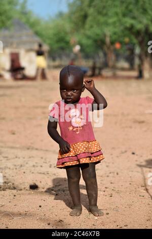 KAMANJAB, NAMIBIA - FEB 1, 2016: Little unidentified Himba girl in bright dress shown in himba tribe village Stock Photo