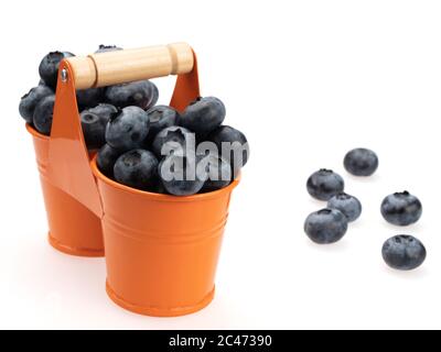 Berries of ripe blueberries in two orange buckets, and scattered around them, on a white background. Stock Photo