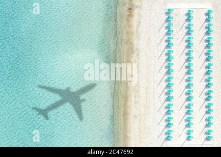 View from above, stunning aerial view of a white sand beach with beach umbrellas and the shadow of an airplane on a beautiful turquoise sea. Stock Photo