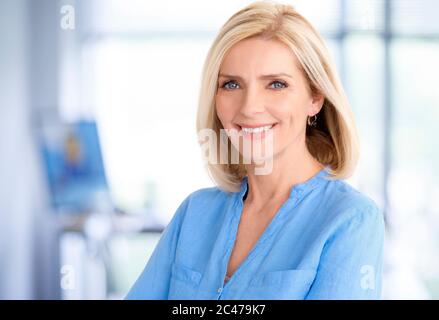 Close-up portrait of beautiful blond businesswoman standing in the office while looking at camera and smiling. Stock Photo