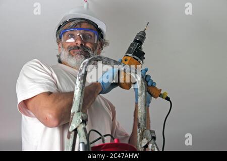 smiling man with electric drill  installing a lamp on the ceiling Stock Photo