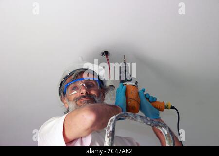 smiling man with electric drill  installing a lamp on the ceiling Stock Photo