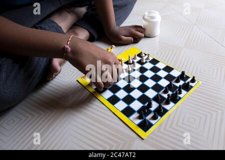 Closeup shot of a person sitting on the white patterned floor and playing chess Stock Photo