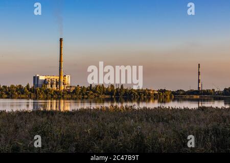 Old Waste incinerator plant with smoking smokestack on Lake bank. The problem of waste processing Stock Photo