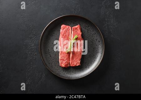 Raw ribeye steak on cutting board with rosemary on black background. Stock Photo