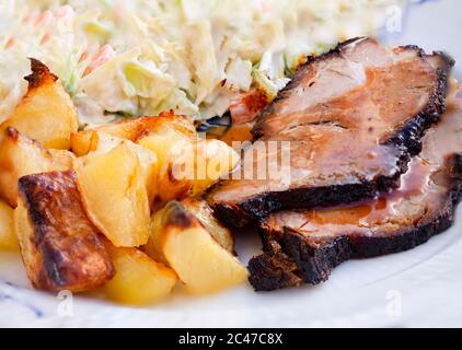 Slices of braised roast pork with bbq gravy, grilled golden pieces of potato and freshly made coleslaw salad. Super close-up image with selective focu Stock Photo
