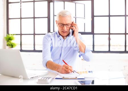 Shot of successful businessman working on laptop and doing some paperwork while sitting at desk. Home office. Stock Photo