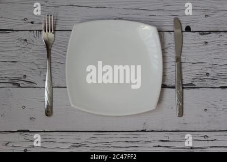 Empty plate, fork and knife over wooden background. Clean plate and cutlery on light background. Top view. Flat lay. Stock Photo