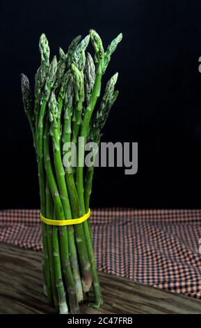 Closeup of a handful of wild asparagus on a wooden cutting board isolated on dark background Stock Photo