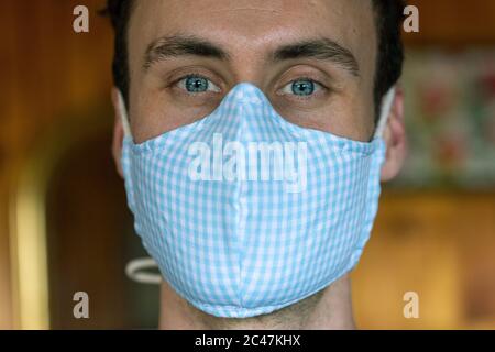 Young male donning deluxe fabric mask front good bone structure blue eyes strong jaw dark hair Stock Photo