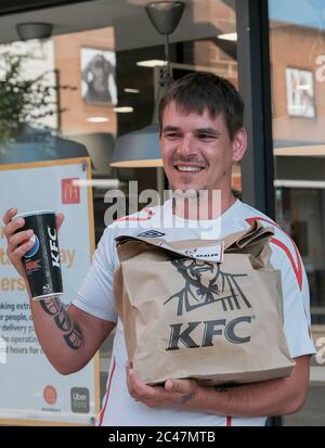 Eastleigh Hampshire, UK. June 24th 2020, Young man with tattoos on arms smiling and happy holding paper kentucky fried chicken and soft drink, Eastleigh, Hampshire, UK Credit: Dawn Fletcher-Park/Alamy Live News Stock Photo