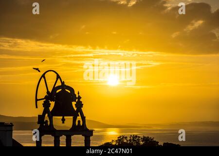 Ardara, County Donegal, Ireland 24th June 2020. The sun sets over the Atlantic Ocean coastal village silhouetting the church bell-tower. Stock Photo