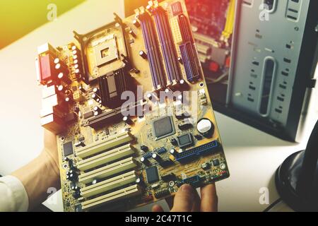 Computer repairman holds motherboard from computer in his hands. Professional PC repair Stock Photo
