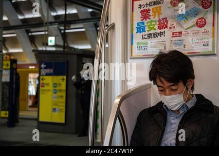 A young man wearing a face mask sits on a Ginza line car. In the background, the subway station with a yellow vehicle stopped on the opposite track. Stock Photo