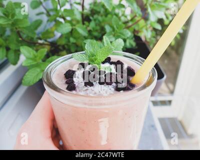 Fresh homemade pink smoothie with dried blueberries, coconut and mint leaves on the top. Healthy diet with fruits. Stock Photo