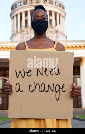 Young african woman wear black face mask stand outdoors holding sign protesting. Stock Photo