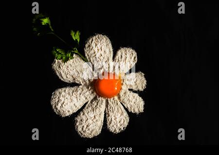 photo of daisies made from flour with egg yolk in the middle on a black background Stock Photo