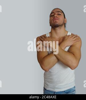 Young hispanic man with gathered hair done bow wearing white sleeveless t-shirt, with his hands on his chest, looking towards the camera with aggressi Stock Photo