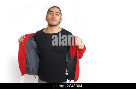 Young hispanic man with gathered hair done in bun wearing black shirt and red jacket, hands opening his jacket, with his eyes towards the camera on wh Stock Photo